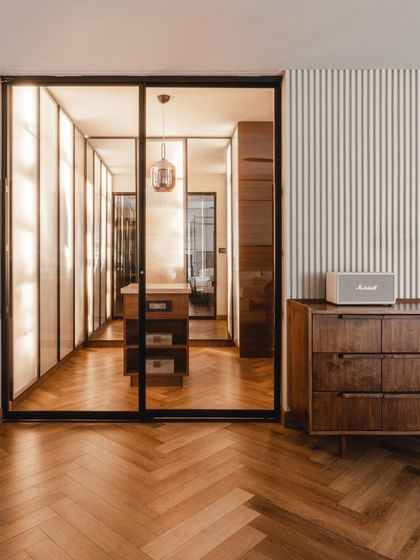 We designed this luxurious walk-in wardrobe with backlit panels that make the entire space glow. The herringbone wooden floor and central storage island add to the opulent, boutique-like feel.