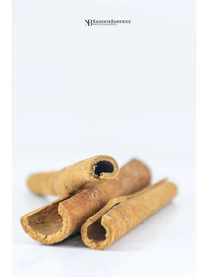 A close-up macro shot of cinnamon sticks on a clean white surface. This minimalist approach highlights the natural texture and detail of the spice. It's a simple yet elegant image for ingredient-focused branding.