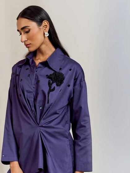 A detailed view of the deep purple draped shirt, highlighting the black floral appliqué and scattered beadwork.