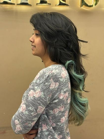 A side profile of a client with long, dark hair and beautiful mint green ends. This is a great example of how to incorporate fashion colors in a subtle yet impactful way.
