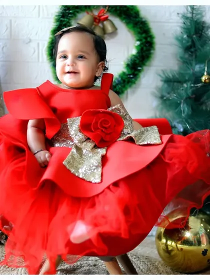 A beautiful baby girl in a stunning red dress, posing in our festive Christmas setup with golden ornaments and a wreath.