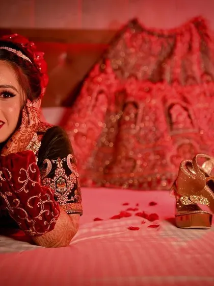 A playful and happy bridal portrait, with the bride resting on her bed next to her wedding lehenga and shoes.