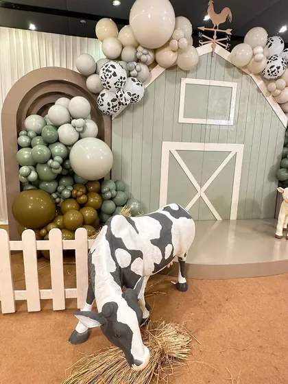 A friendly cow prop grazes on hay in front of the stylish sage green barn, adding a touch of realism to this chic farm-themed party.