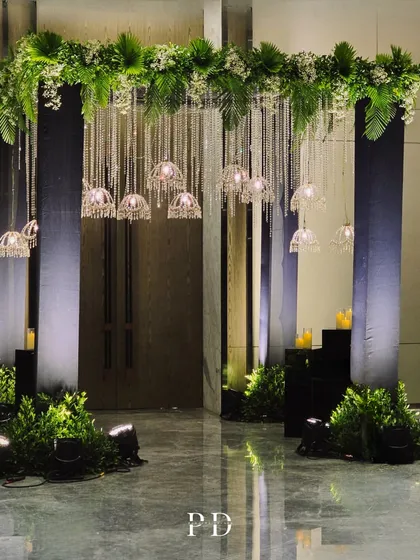 A glamorous Sangeet entrance featuring a curtain of hanging crystals and crystal-domed chandeliers, framed by lush greenery. This design is all about sparkle and modern elegance.