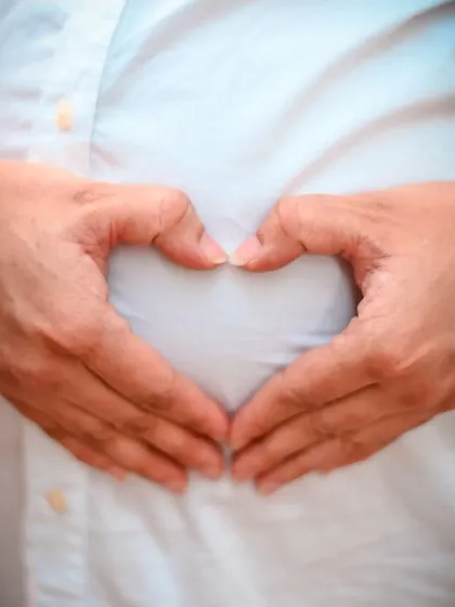 A simple and iconic maternity photo. The mother-to-be forms a heart with her hands over her baby bump, a universal symbol of the immense love she already feels for her child.