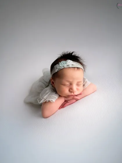 A newborn baby rests her head on her hands against a clean, white textured background. The simplicity of this shot draws all attention to the baby's peaceful expression and delicate features.