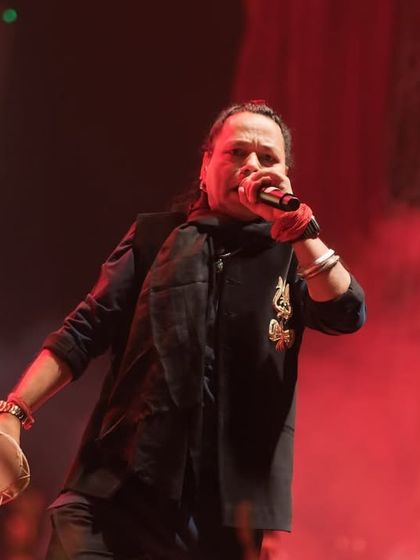 Kailash Kher lost in his performance, singing with raw passion. The red lighting enhances the intensity of the moment, making for a powerful concert photograph.