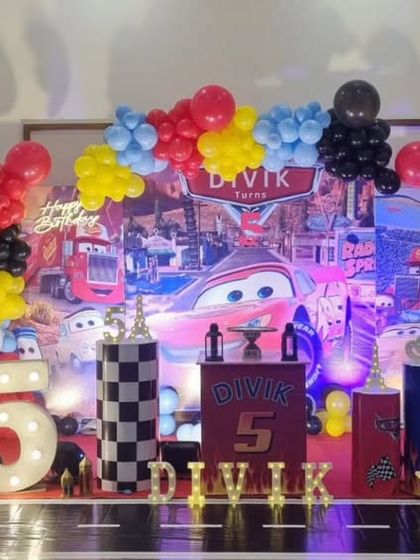 A full stage setup for a 'Cars' themed 5th birthday, featuring a vibrant backdrop and numerous character and racing props.