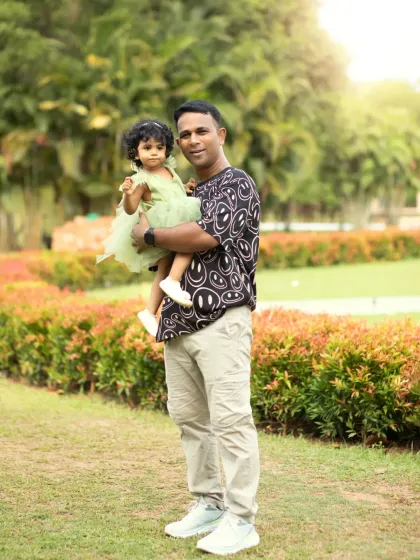 A proud father holds his little girl in his arms during their outdoor family photoshoot in a lush green park.