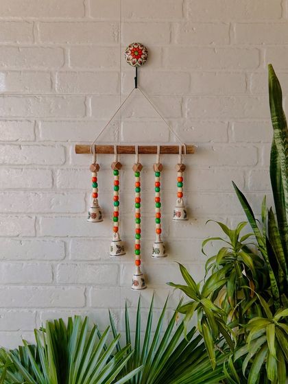 A closer look at our beads and bells handmade wall hanging. This one is in the 'Marigold' variant, with orange and green wooden beads. It comes with a ceramic wall hook and makes an excellent housewarming gift.