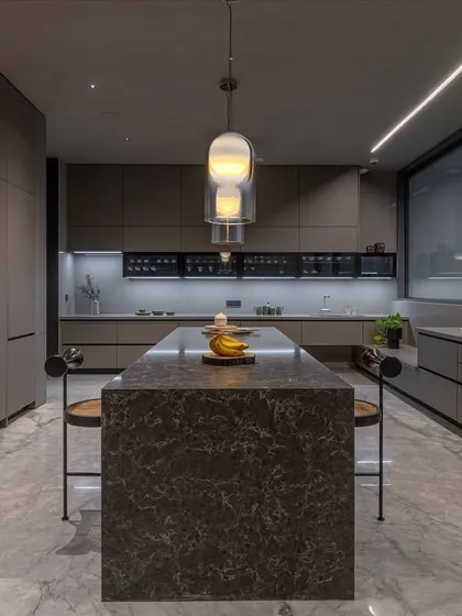 A front view of the sculpted stone island, which acts as the kitchen's dramatic focal point. Its substantial form is balanced by the sleek, minimalist cabinetry.