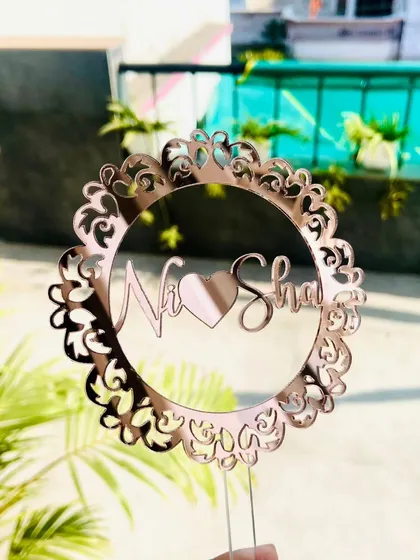 The "Ni-Sha" mandala topper held outdoors, with the sunlight catching the reflective rose gold finish.