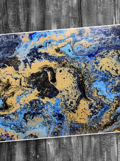 This fluid art piece showcases a dramatic interplay of blue, black, and gold, demonstrating how to create cosmic or galaxy-like effects with liquid acrylics.