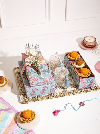 Our Rakhi hamper, featuring Mithai Tartlets, beautifully wrapped gift boxes, and decorative jars, all arranged on a rustic tray.