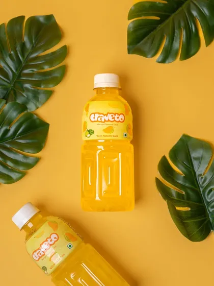 A mango-flavored drink styled with tropical leaves on a bright yellow background. The color harmony and props immediately suggest a refreshing, summery taste.