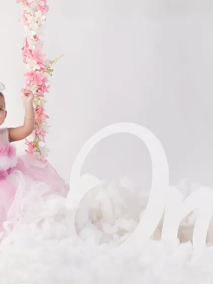 Baby Gia celebrating her first birthday, sitting happily next to a floral swing and a large "One" sign.
