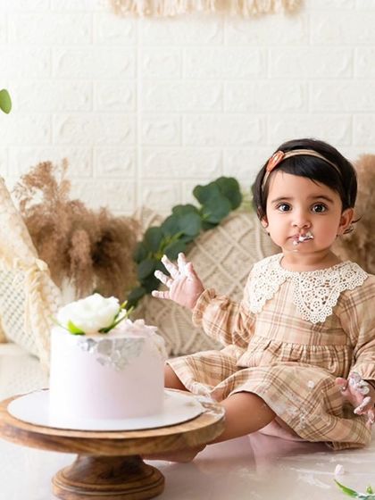 This shot shows the baby sitting with her cake in a fully styled boho setup, featuring a teepee and neutral tones.