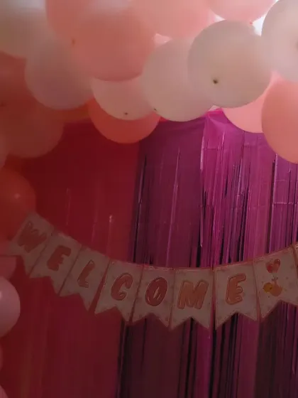 A close-up of the "Welcome Baby" banner from a home decoration setup. The pink shimmer curtains and pastel balloons add a touch of sparkle to the celebration.