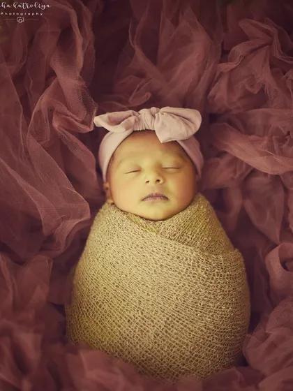 This 14-day-old doll is sleeping peacefully, wrapped in a rustic burlap-style swaddle and a pink bow headband.