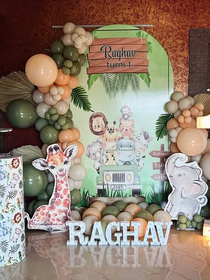 A modern jungle theme for a first birthday. This setup uses muted green and peach balloons, a large marquee number '1', and cute animal cutouts for a stylish take on the safari theme.