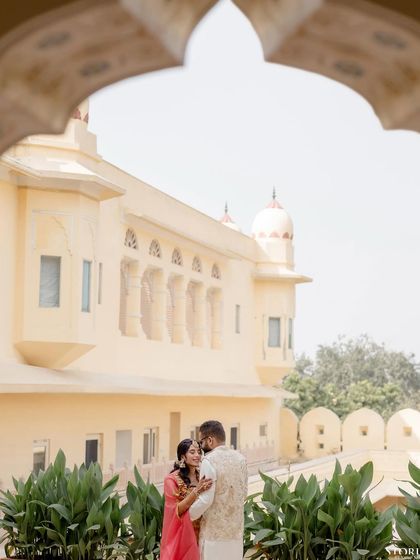 The couple framed within a traditional Rajasthani archway, creating a beautiful composition that blends romance with heritage architecture.