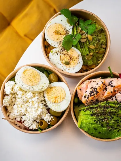 A trio of healthy takeaway bowls, shot from above. The composition highlights the different toppings and colors, showing off the menu's variety.