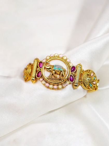 An ornate, traditional elephant-motif bracelet styled on a white silk background. The soft fabric enhances the perceived value and luxury of the piece.
