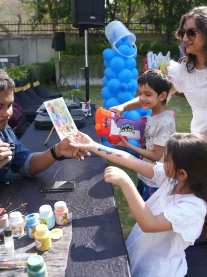 Creative stations like temporary tattoo and face painting are a great way to keep kids engaged. Our artist is seen here painting a colorful design on a child's arm at a fun outdoor pool party.