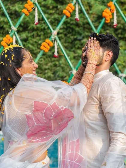A happy bride playfully applies Haldi to the groom. We design our decor, like this marigold-adorned backdrop, to be the perfect setting for these fun moments.
