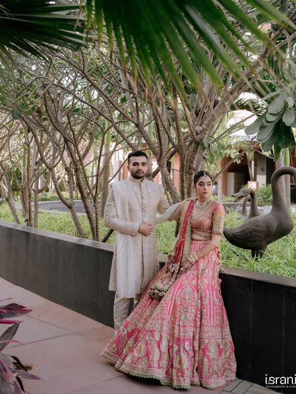 A full-length portrait of the couple, showcasing their stunning wedding attire against the modern architecture and greenery of the venue.