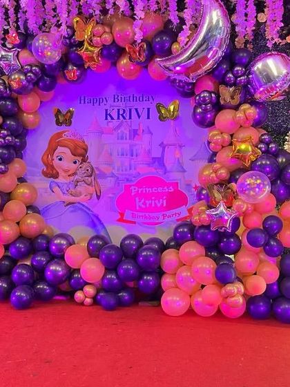 A "Sofia the First" princess theme for a first birthday. The purple and pink balloon arch complements the custom backdrop and light-up number '1'.