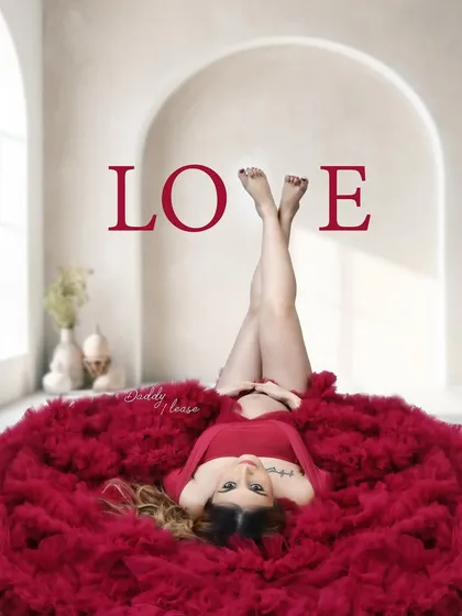 A creative top-down shot of a mother-to-be lying on a bed of red tulle. This artistic pose is a unique way to capture the beauty of pregnancy.