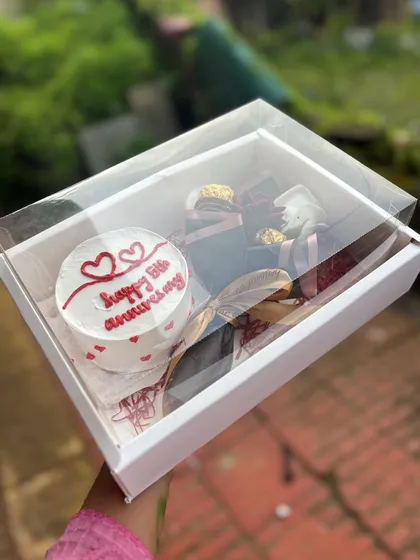 A sweet anniversary gift box. This features a bento cake with "Happy 5th Anniversary" written on it, along with Ferrero Rocher chocolates and a golden spoon, all elegantly packaged.
