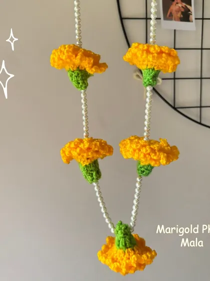 A handmade crochet Marigold Phool Mala (genda phool) hanging on a wall grid, perfect for adding a festive touch to your home.