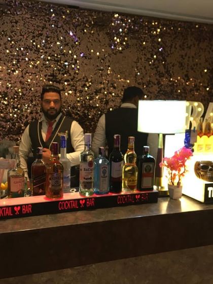 A full bar counter against a sparkling sequin backdrop, with a bartender ready to serve.