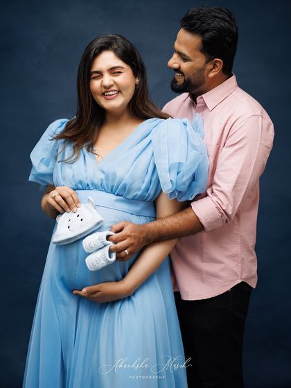 A playful and sweet maternity portrait. The expecting parents hold up tiny baby shoes, a joyful and classic way to announce their growing family.
