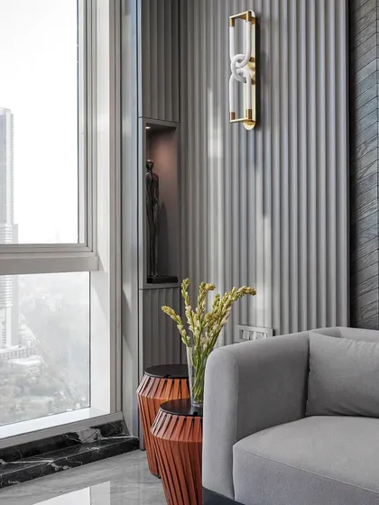 This waiting area combines comfort with style, featuring a plush grey sofa, textured walls, and a unique wall sconce. The large window offers natural light and a beautiful view of the city.