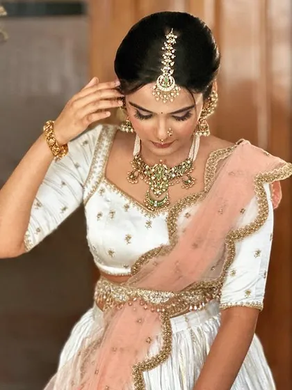 A bride in a white and peach half-saree. Her custom white blouse features delicate embroidery, creating a soft and elegant look for her ceremony.