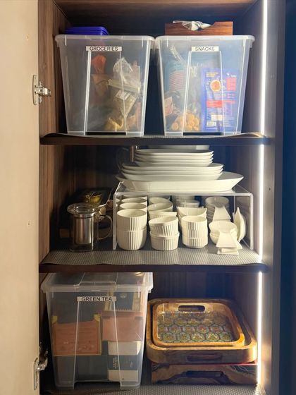 This cabinet uses clear bins to group items like groceries, snacks, and green tea. Below, we've used a riser to double the storage space for plates and cups, making everything visible.