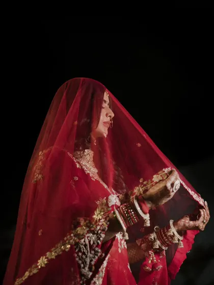 A beautiful bridal portrait under a red veil. This classic shot captures the bride's anticipation and the rich traditions of an Indian wedding.