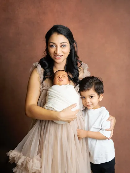 A beautiful portrait of a mother with her two sons. She holds her newborn while her toddler stands close, creating a lovely image of her life with her boys.