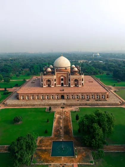 A wide aerial photograph of Humayun's Tomb, capturing the full monument and its symmetrical gardens. This shot highlights the tomb's grandeur and its peaceful setting within a lush green landscape in the heart of Delhi.