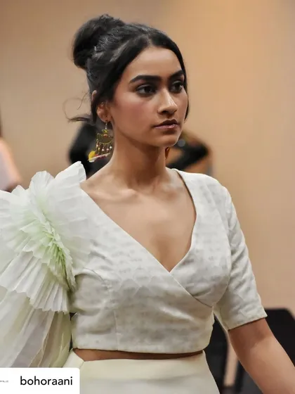 A backstage glimpse of a model wearing our custom white wrap blouse. The focus is on the single, exaggerated ruffled sleeve made from delicate, pleated organza, a key feature of our design.