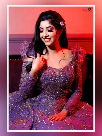 An indoor portrait with dramatic, colorful lighting. The model's joyful expression is highlighted by the warm red and purple tones, showcasing our ability to create glamorous, high-fashion looks for evening events or engagement parties.