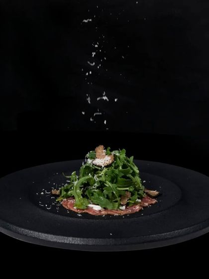 A chef's final touch, grating fresh cheese over a salad of rocket leaves. It is these small details that elevate a simple dish to something special.