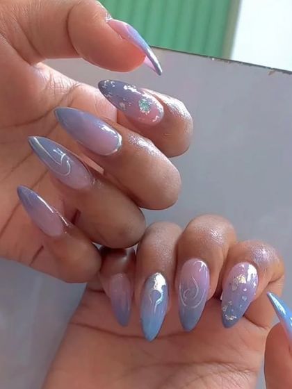 A dreamy pastel set in shades of blue and lavender with subtle silver swirls and glitter accents on stiletto nails.