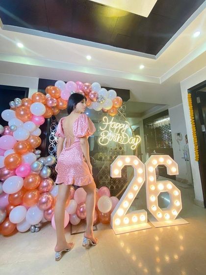 The birthday girl looking fabulous in front of her custom 26th birthday backdrop. The pink, orange, and white balloon arch perfectly complements her outfit.