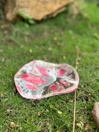 A stoneware wall piece with a striking pink and black abstract design. While it can be hung on a wall, it could also serve as a unique decorative platter on a coffee table.