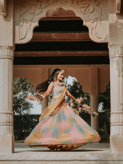 A beautiful solo portrait of the bride twirling in her multi-colored Haldi lehenga. This shot captures her happiness and the beauty of her outfit against an elegant architectural backdrop.