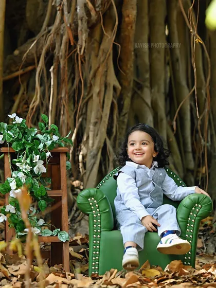 A candid shot of the little boy sitting in a miniature green armchair during his outdoor photoshoot.